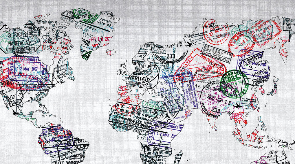 Full shot of a world map, likely a graphic design or print, overlaid with numerous passport stamps of varying colors and sizes. The stamps are densely clustered across the map, covering almost all landmasses.  The colors of the stamps include reds, blues, greens, purples, and other hues, suggesting different countries or regions.  Each stamp has text and symbols, typical of immigration and visa records, but the specific meanings are not discernible from this view. The map itself is a white/light grey on a textured background, possibly linen, that gives the image some tactile visual depth.  The outline of the world's continents is clearly visible beneath the stamps, as if the map is layered over a base image. The overall effect is one of visual density and a sense of global travel and immigration.