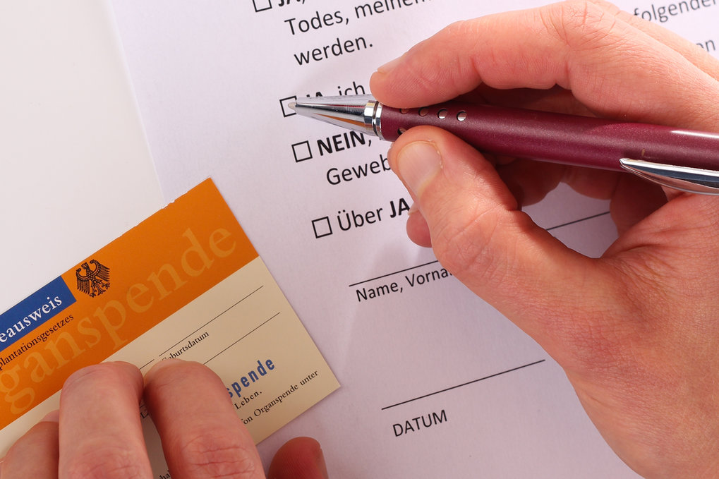 The picture shows a hand filling out an application for a German organ donor card.