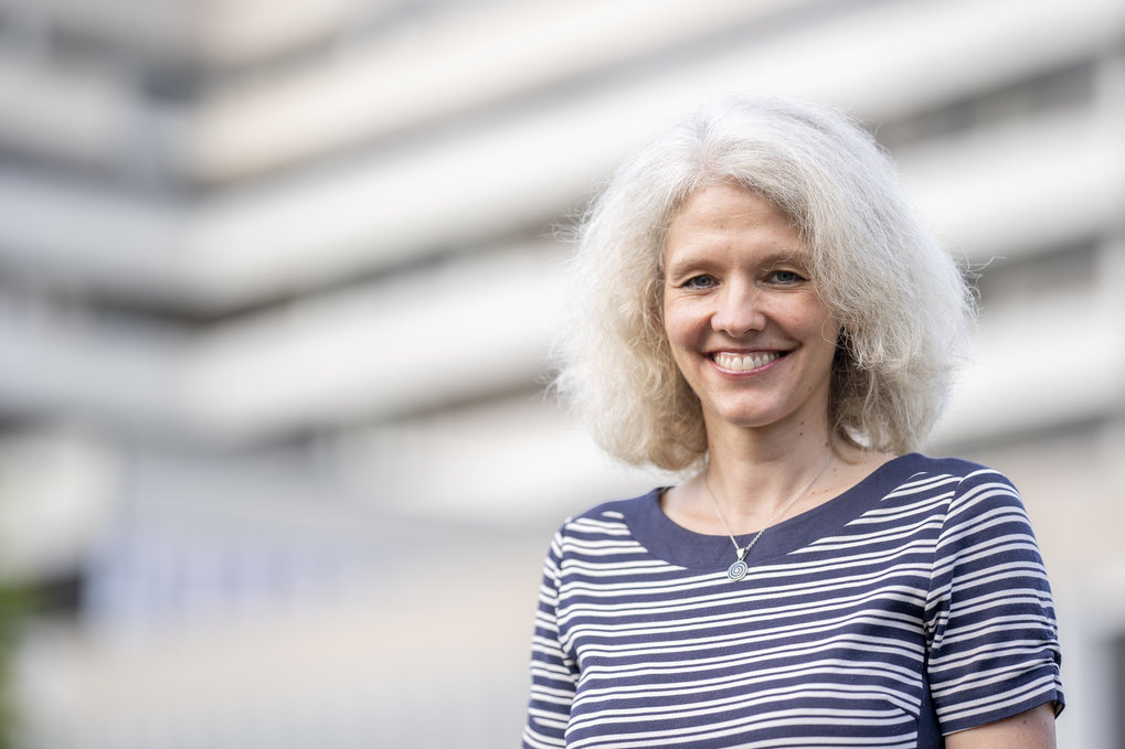 A portrait of Bettina Lotsch, Director at the Max Planck Institute for Solid State Research in Stuttgart, looking at the camera and smiling. She has shoulder-length white hair and is wearning a T-shirt with white and blue stripes.