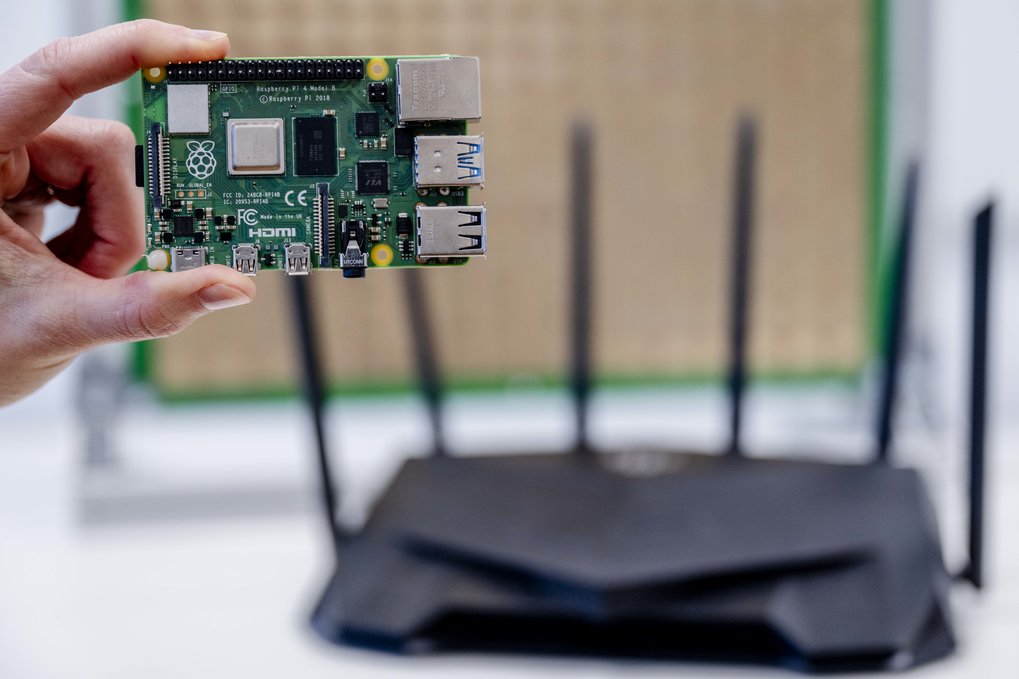 A hand holding a Raspberry Pi board in front of a router.